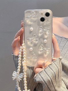 a woman holding up her phone case with pearls and bows on it