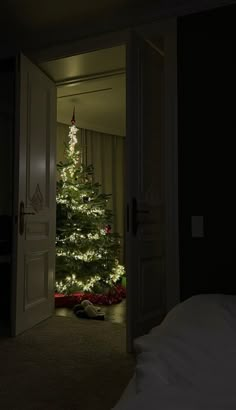 a lit christmas tree in the corner of a room with an open door leading to another room