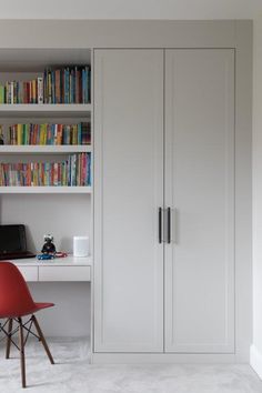 a white bookcase with books and a red chair next to it in front of a computer desk