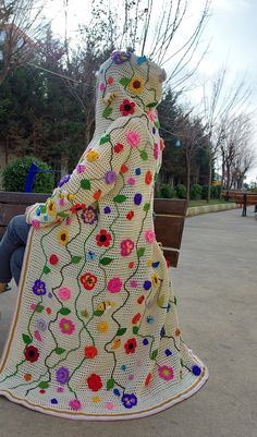 a woman sitting on a park bench covered in a crocheted blanket with flowers