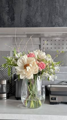 a vase filled with white and pink flowers on top of a counter next to a toaster oven