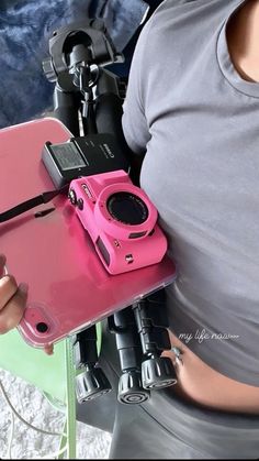 a woman holding a pink camera in her hand and some other equipment on the ground