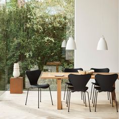 a dining room table with chairs and a vase on the side, in front of a large window