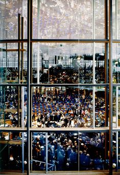 a large room filled with lots of people standing in front of glass walls and windows