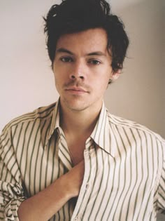 a young man wearing a striped shirt is posing for the camera with his hand on his chest