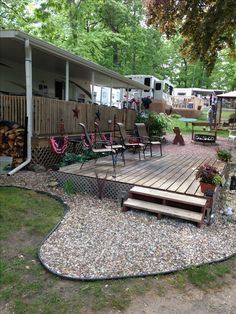 a house with a deck and chairs in the yard next to some firewood stacked on top of each other