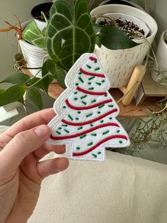 someone is holding up a christmas tree patch in front of some plants and potted plants