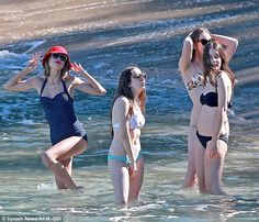 three women in bathing suits are standing in the water at the beach and one is holding her head