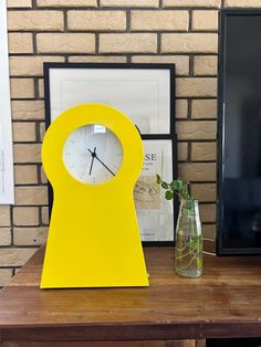 a yellow clock sitting on top of a wooden table next to a vase with flowers