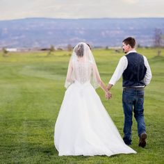 a bride and groom holding hands walking through the grass in front of a golf course