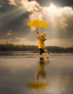 a child in yellow raincoat holding an umbrella over his head and running across the water