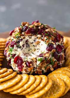 a cheese ball with cranberries and pecans is on a platter surrounded by crackers