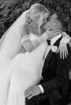 a bride and groom kissing in front of a bush on their wedding day, black and white photo