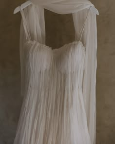 a wedding dress hanging on a hanger in front of a wall with sheer curtains