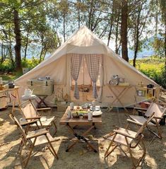 a tent set up in the woods with four chairs and an outside table that has food on it