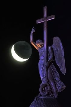 a statue of an angel holding a cross with the moon in the background