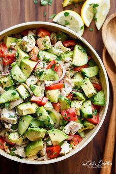 a bowl filled with cucumber and tomatoes next to wooden spoons on a table