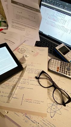 two laptops and a calculator sitting on top of a desk covered in papers