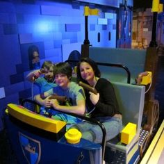 three people sitting on a roller coaster in a legoland ride at night time,