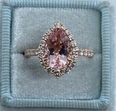 a pink diamond ring in a blue box with diamonds on the sides and an oval shaped center