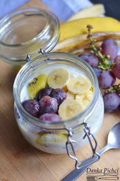 a glass jar filled with fruit sitting on top of a wooden cutting board next to bananas and grapes