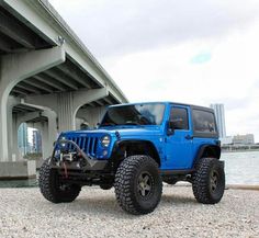 a blue jeep parked under a bridge next to the water with its front wheels off