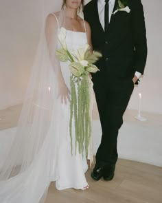 a bride and groom posing for a photo in front of a white wall with candles