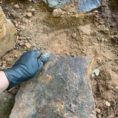 a person wearing black gloves standing on top of a dirt covered ground next to rocks