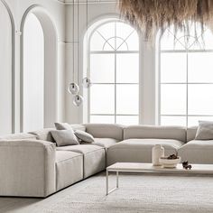 a living room with white walls and large windows in the corner, including a sectional couch