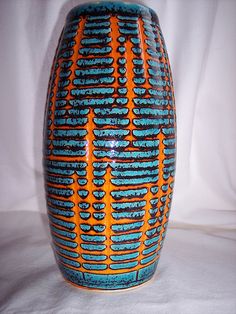 an orange and blue vase sitting on top of a white table