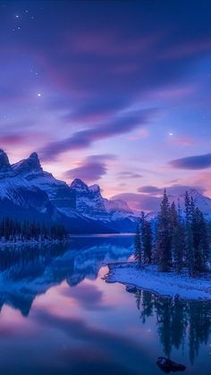 the mountains are covered in snow as the sun sets over a lake with trees on both sides