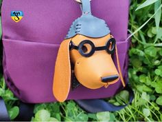 a purple backpack with a dog wearing glasses on it's face and a keychain hanging from the front