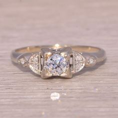 an antique style diamond ring on a wooden table with diamonds around the band and center stone