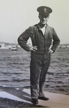 an old black and white photo of a man in uniform standing by the water with his hands on his hips