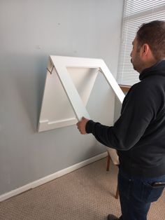 a man is holding up a large white triangle shaped object in the corner of a room