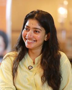 a woman sitting at a table with a smile on her face and long dark hair