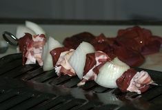 some meat and onions are being cooked on a bbq grill with toothpicks