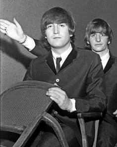 two young men sitting next to each other in front of a chair and one holding his hand out