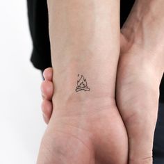 two hands holding each other with a small tattoo on the wrist that has a campfire in it