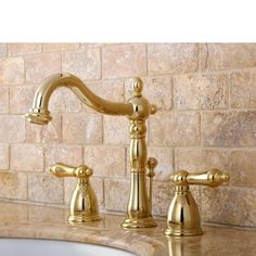 a gold faucet with two handles on a marble countertop in front of a brick wall