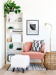 a living room with a pink chair and white bookshelf filled with plant life