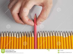 a hand holding a pencil over a row of orange and yellow pencils on a gray background