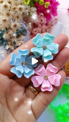 three small flowers are in the palm of someone's hand, one is blue and one is pink