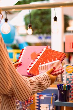 a woman is holding several notebooks in her hands and looking at the book on the table