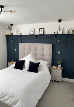 a white bed sitting in a bedroom next to a wall with framed pictures on it