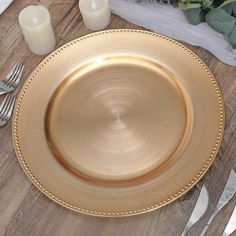 a gold plate sitting on top of a wooden table next to silverware and candles