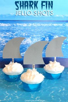 three cupcakes with white frosting in front of the ocean and shark fin