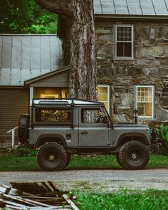 a gray jeep parked in front of a stone house next to a tree and grass