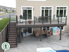 a deck with chairs and a table next to a pool in front of a house