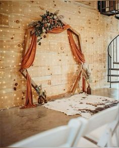 a wedding arch with flowers and candles on the floor in front of a wooden wall